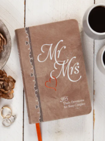 Brown notebook with 'Mr & Mrs' on a wooden surface with coffee cups and decorative items.